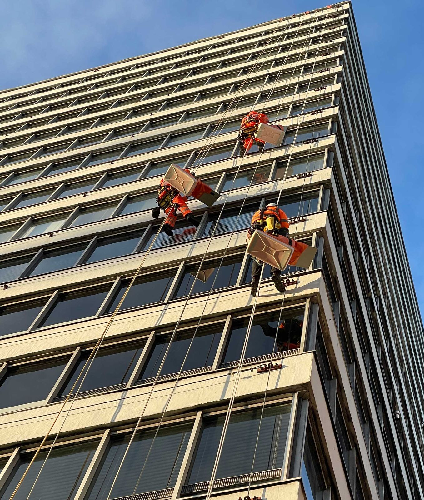 Abseilers on ropes fitting panels over the window frames of a tower