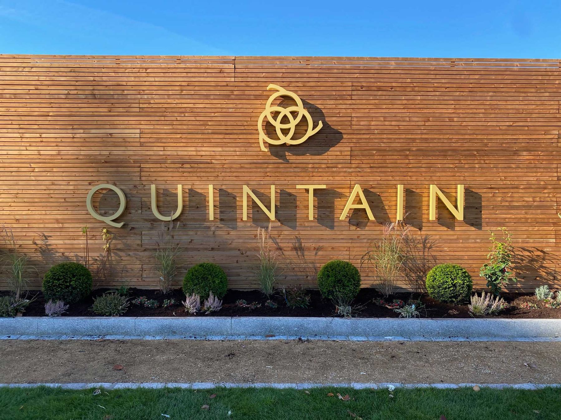 Timber-clad entrance wall with gold Quintain lettering above planting